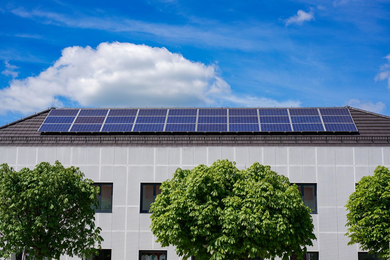 our-journey-03 Energy-efficient building topped with solar panels and surrounded by lush trees.