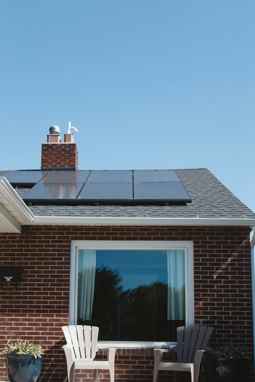experience-img Vivint Solar - Solar Panels on roof of brick home with window and Adirondack chairs.