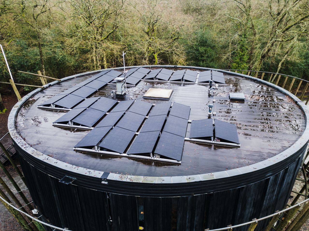 our-journey-02 Aerial view of a round rooftop with solar panels surrounded by trees, promoting renewable energy.